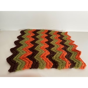 May include: A crocheted blanket with a chevron pattern in shades of brown, green, and orange.