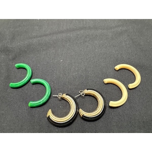 May include: A collection of hoop earrings in various colors. Two pairs of earrings are black and gold, two are green, and two are cream-colored. The earrings are arranged on a dark surface.