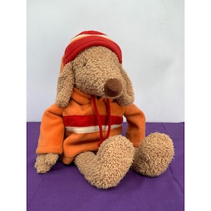 May include: A plush brown dog wearing an orange hoodie with red and white stripes and a red and orange striped hat.
