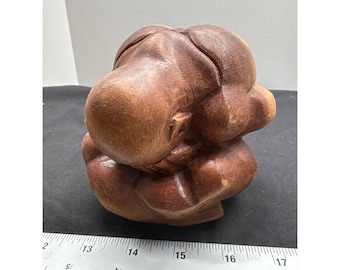May include: A carved wooden sculpture of a seated figure, with a smooth, polished surface. The sculpture is a warm brown color and appears to be hand-carved. The figure is in a seated position, with the head resting on the knees. The sculpture is approximately 6 inches long.