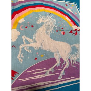 May include: A blue and purple fabric with a white unicorn standing on a purple cloud. The unicorn is surrounded by stars and a rainbow.