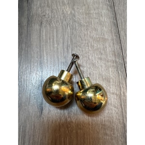 Puede incluir: Dos pomos esféricos para armarios con un acabado metálico en tono dorado pulido. Cada pomo presenta una cabeza lisa y redondeada, junto con un tornillo roscado de metal que se extiende desde la base para fijarlo a muebles o cajones.
