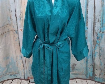 May include: A teal satin robe featuring a tonal jacquard pattern with a subtle sheen. The garment has long sleeves, a shawl collar, and a matching fabric tie belt at the waist, creating a wrap-style closure with a smooth, flowing drape.