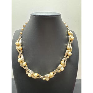 May include: A vintage gold-tone necklace with faux pearls. The necklace features a series of cream-colored faux pearls interspersed with ornate, leaf-like gold metalwork. The necklace is displayed on a black mannequin.