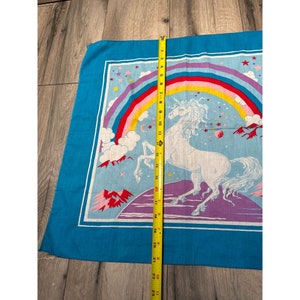 May include: A blue bandana with a white unicorn standing on a purple and blue planet. The unicorn is surrounded by a rainbow and stars.