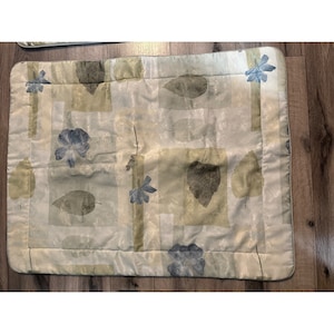 May include: A cream-colored throw pillow with a subtle leaf and flower pattern in shades of green and blue.