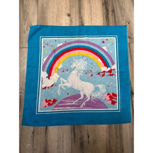 May include: A blue bandana with a white unicorn standing on a purple and pink rainbow. The unicorn is surrounded by stars and clouds. The bandana has a white border.