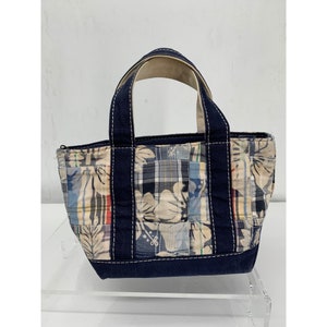 May include: A small, navy blue tote bag with a patchwork design featuring floral and plaid patterns. The bag has two top handles and a zip closure.