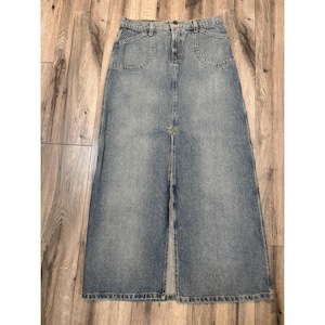 May include: A light-wash denim maxi skirt with a front slit. The skirt features two front pockets and a button and zipper closure. The skirt is made of a sturdy denim material and has a classic, vintage style.