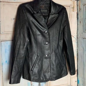 以下が含まれることがあります： クラシックなデザインの黒いレザージャケット。ノッチドラペル、3つボタン留め、フロントポケット2つが特徴です。「Wilsons Leather」と書かれたラベルが付いています。
