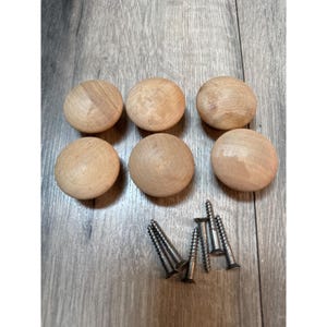 Puede incluir: Seis pomos redondos de madera de color claro para armarios con un acabado natural y suave. Cada pomo tiene un orificio central para el montaje. Se incluyen seis tornillos metálicos de color plateado con vástagos roscados para los muebles.
