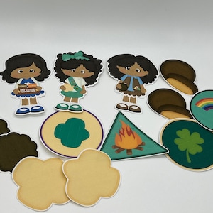 May include: A collection of Girl Scout-themed paper cutouts. The cutouts include three cartoon girls, badges, cookies, and other related images. The color palette includes brown, green, blue, yellow, and orange.