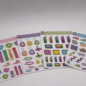 May include: Four sheets of stickers with a 90s theme. The stickers feature images of cell phones, game controllers, cameras, and other 90s icons. The stickers are on a white background with colorful confetti.