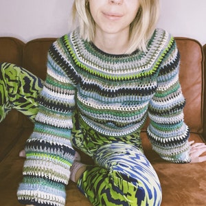 Puede incluir: Una mujer con un suéter de crochet a rayas verdes, azules y blancas con pantalones de estampado de cebra verde y azul.