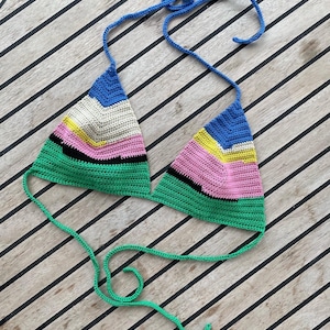 Pode incluir: Um top de biquíni de crochê colorido com listras verdes, azuis, rosa, amarelas e pretas. O top tem formato triangular e alças ajustáveis.