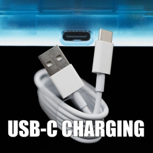Puede incluir: Un cable de carga USB-C blanco con un conector USB-A en un extremo y un conector USB-C en el otro extremo. El cable est&aacute; enrollado y el conector USB-C est&aacute; conectado a un dispositivo.