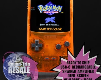 Könnte beinhalten: Eine leuchtend orangefarbene Game Boy Color Handheld-Videospielkonsole mit einem Schwarzweiß-Bildschirm, auf dem das Logo von Pokemon Crystal Version angezeigt wird. Die Konsole hat eine silberne Frontplatte mit Knöpfen und einem Steuerkreuz.