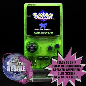 May include: A transparent neon green Game Boy Color handheld game console. The screen displays the "Pokémon Crystal Version" title screen. The console has a D-pad, A and B buttons, and a speaker amplifier. The text "Round-Trip RESALE" is also visible.