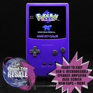 May include: A purple Game Boy Color console displaying the "Pokémon Crystal Version" game. The screen shows the game's logo and a silhouette of a Pokémon. The console has a directional pad, A and B buttons, and a "Nintendo" logo.