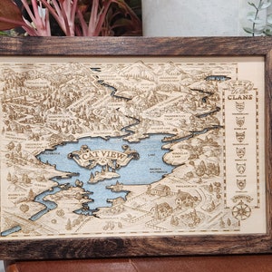 May include: A wooden map of Cat View, a fictional location, with a blue lake and surrounding forest. The map is framed in a dark wood frame and includes a compass and a list of clans.