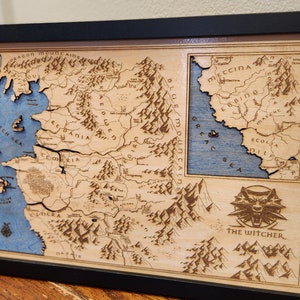 May include: A wooden map of the Continent from The Witcher video game series. The map is framed in black and features a blue and brown color scheme. The Witcher logo is in the bottom right corner.
