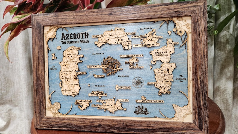 May include: A wooden map of the fictional world of Azeroth, from the Warcraft video game series. The map is framed in a dark wood frame and features a blue background with various islands and continents labeled with names like "The Dragon Isles", "Eastern Kingdoms", and "The Broken Isles".