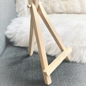 Puede incluir: Un peque&ntilde;o caballete de madera, hecho de madera marr&oacute;n claro, con un dise&ntilde;o simple. Es un caballete de mesa, perfecto para exhibir peque&ntilde;as obras de arte o fotos.