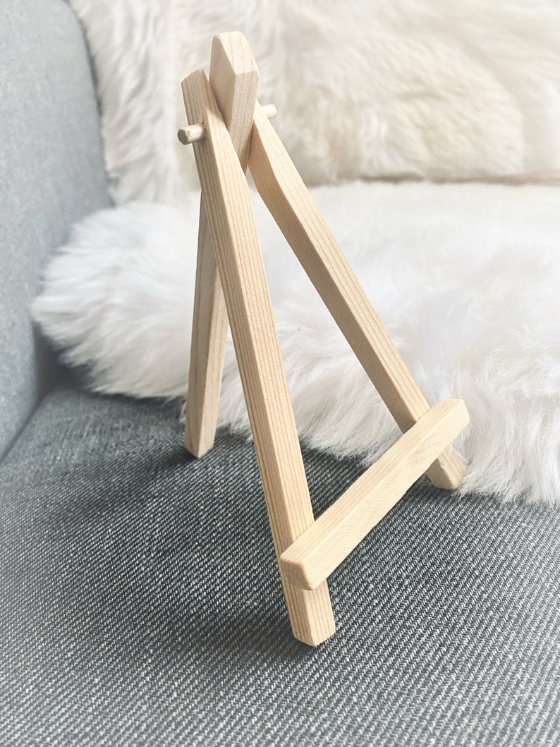 Puede incluir: Un peque&ntilde;o caballete de madera, hecho de madera marr&oacute;n claro, con un dise&ntilde;o simple. Es un caballete de mesa, perfecto para exhibir peque&ntilde;as obras de arte o fotos.