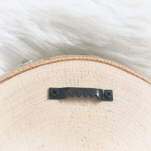 Puede incluir: La parte posterior de un letrero redondo de madera con un gancho de metal negro para colgar.