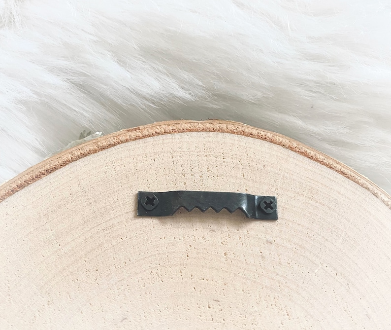 Puede incluir: La parte posterior de un letrero redondo de madera con un gancho de metal negro para colgar.