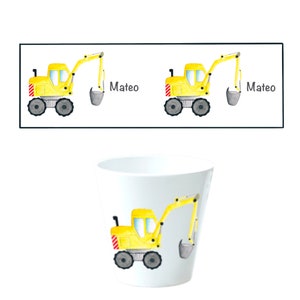 May include: A yellow toy excavator with a gray bucket is on a white cup. The cup has the name "Mateo" written on it.