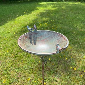 May include: A rustic green metal bird bath with a decorative stand. The bath has three small bird figurines on the rim.