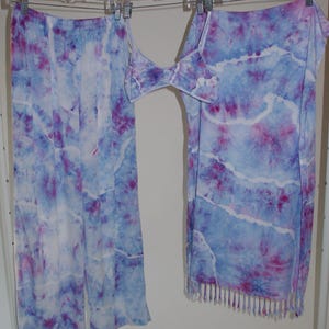 May include: A tie-dye set of clothing with a skirt, pants, and a top. The clothing is a light blue color with pink and white tie-dye patterns. The skirt has a fringe trim.