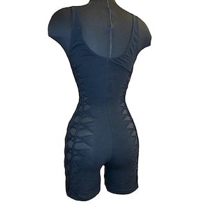 May include: Black one-piece garment with a cutout design on the sides. The garment is sleeveless and has a scoop neck.