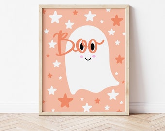 May include: A framed wall art print featuring a white ghost character with black eyes and pink cheeks on a peach background. The word Boo is written in orange script, and the design is decorated with scattered white and orange stars throughout.
