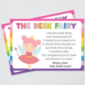 May include: A pink and purple card with a rainbow border. The card features a cartoon fairy with a pink dress and a crown. The text on the card reads "THE DESK FAIRY" and includes a poem about a desk fairy who visited a classroom and found a tidy desk.