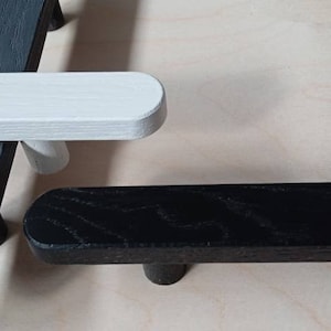 May include: Three wooden drawer pulls, one painted white, one black, and one dark gray. The pulls are all rectangular with rounded edges.