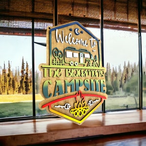 May include: Welcome to The Back Forty Campsite sign with a woodgrain background and a colorful gradient. The sign features a cartoon camper van, trees, and a campfire with marshmallows.