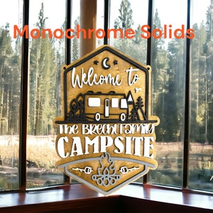 May include: A wooden sign with a welcome to the Brecht family campsite message. The sign is painted in brown, black, and white with a camper van, trees, and a campfire graphic.