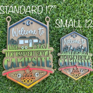 May include: Two wooden signs with a camping theme. The larger sign is 17 inches and the smaller sign is 12 inches. Both signs have a welcome to message, a family name, and the word campsite. The signs are painted in a gradient of green, blue, and red.