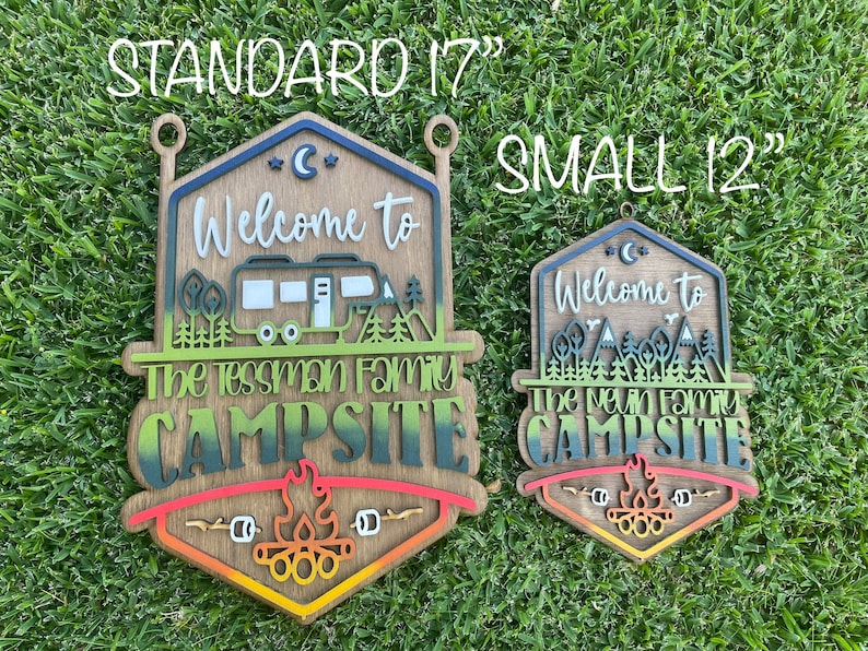 May include: Two wooden signs with a camping theme. The larger sign is 17 inches and the smaller sign is 12 inches. Both signs have a welcome to message, a family name, and the word campsite. The signs are painted in a gradient of green, blue, and red.