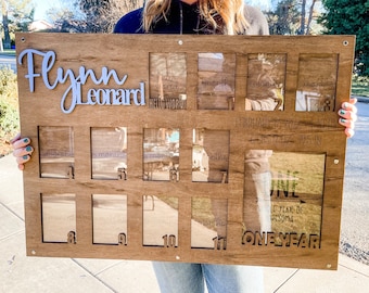 May include: A wooden photo frame with 11 clear plastic picture slots for a baby's first year. The frame is engraved with the name "Flynn Leonard", the date "February 17, 2022", the time "1:48 PM", the weight "6 lbs 7 oz", the length "19.5 in", and the words "Hello World", "One Year", and "One Year of Awesome".