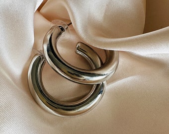 May include: A pair of silver hoop earrings. The earrings are thick and have a smooth, polished finish.