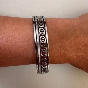 Puede incluir: Pulsera de brazalete de plata con un diseño decorativo de eslabones de cadena.