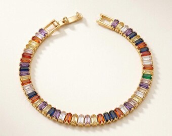 May include: A gold-tone bracelet featuring a continuous row of rectangular baguette-cut stones in a variety of colors including blue, purple, orange, yellow, and clear. The bracelet includes a metal clasp mechanism at the top opening.