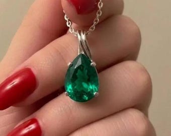 May include: A teardrop-shaped green gemstone pendant set in a silver-toned metal prong setting. The pendant hangs from a delicate silver-toned chain. The gemstone features a faceted surface that reflects light, showcasing a deep emerald green hue.