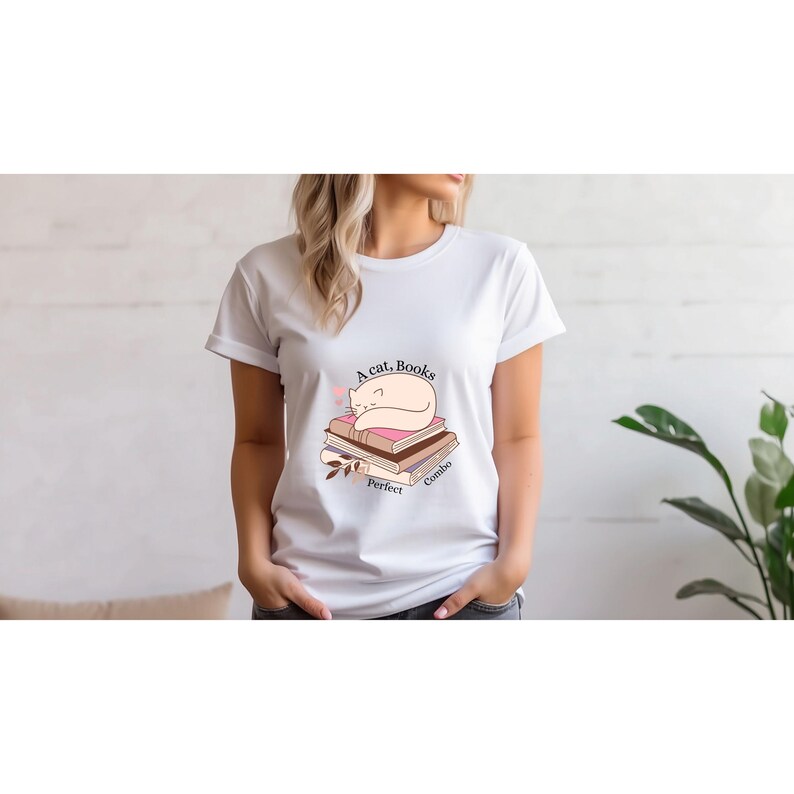 May include: White t-shirt with a graphic of a sleeping cat on a stack of books. The text on the shirt reads "A cat, Books, Perfect Combo" in a soft, feminine font. The design features muted pink and brown tones.