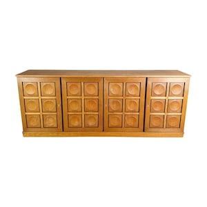May include: A light brown wooden cabinet with four doors. Each door features a grid pattern of squares and circles. The cabinet is rectangular and sits low to the ground, suitable for a living room or dining area.