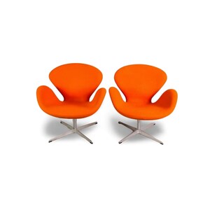 Könnte beinhalten: Zwei orangefarbene Sessel im modernen Stil mit einer markanten schwanenartigen Form. Die Stühle haben eine geschwungene Rückenlehne und Sitzfläche und sind auf einem silbernen, sternförmigen Fuß montiert. Der Hintergrund ist weiß.