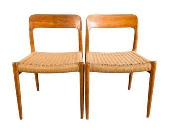 May include: Two wooden chairs with woven seats. The chairs have a light brown finish and a simple, mid-century modern design. The seats are made of a light tan woven material, and the backs have a rectangular cutout.
